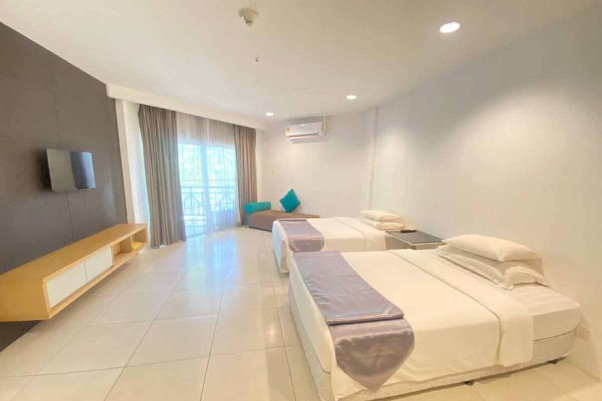 A hotel room with two beds, a TV, a window with curtains, and a wooden bench.
