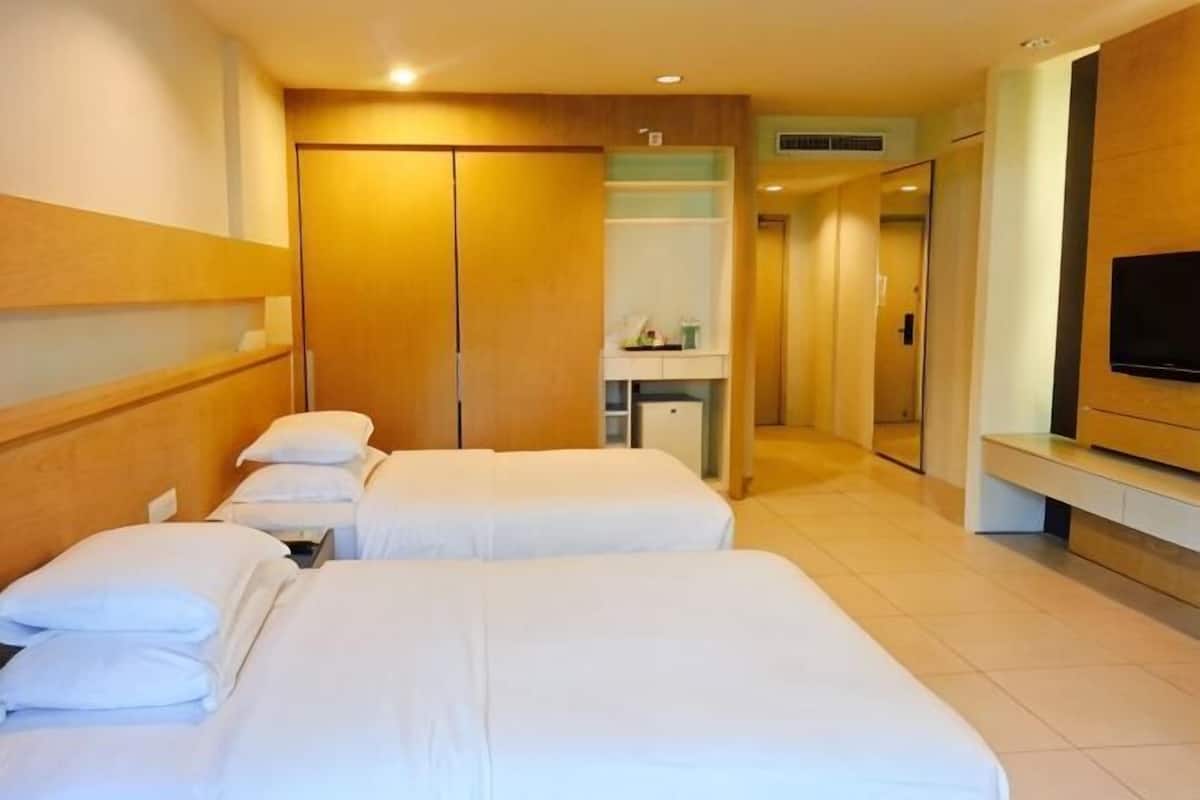 A hotel room with two beds, a TV, a wardrobe, and a bathroom visible in the background.