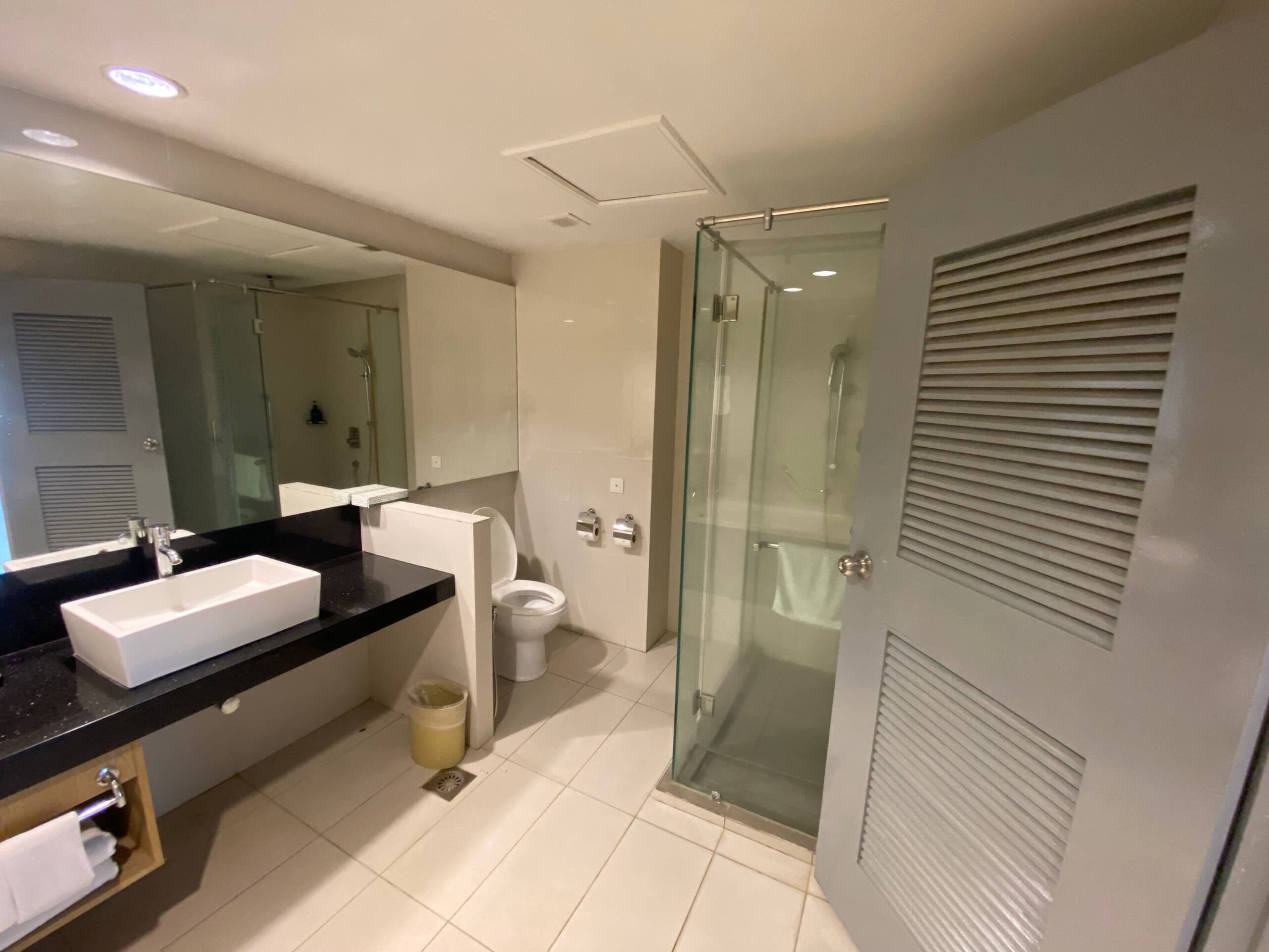 A modern bathroom with a large mirror, a sink, toilet, and a glass-enclosed shower.