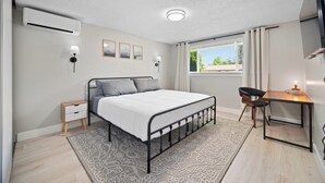 Een moderne slaapkamer met een bed, nachtkastje, lamp en bureau met stoel.