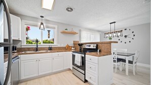 Een moderne keuken met witte kasten, een tegelwand en een eethoek met witte stoelen en een tafel.