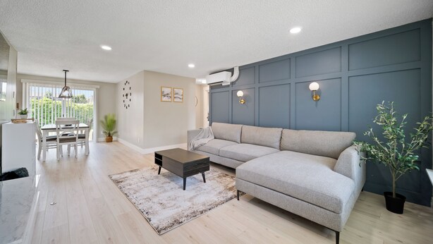 Een moderne woonkamer met een grijze bank, een salontafel en een eethoek met een tafel en stoelen.