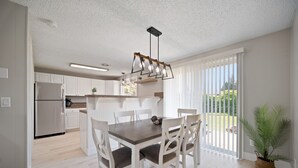 Een moderne keuken met witte kasten, een houten eettafel en een hanglamp.