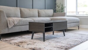 Een moderne woonkamer met een grijze modulaire bank, een donker houten salontafel met lades en een vloerkleed met dessin.