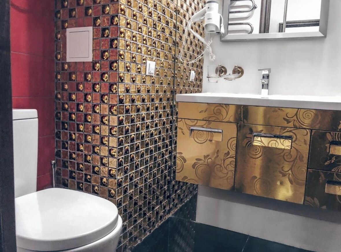 A bathroom with a toilet, a sink, and a mirror. The walls are decorated with a mosaic pattern.