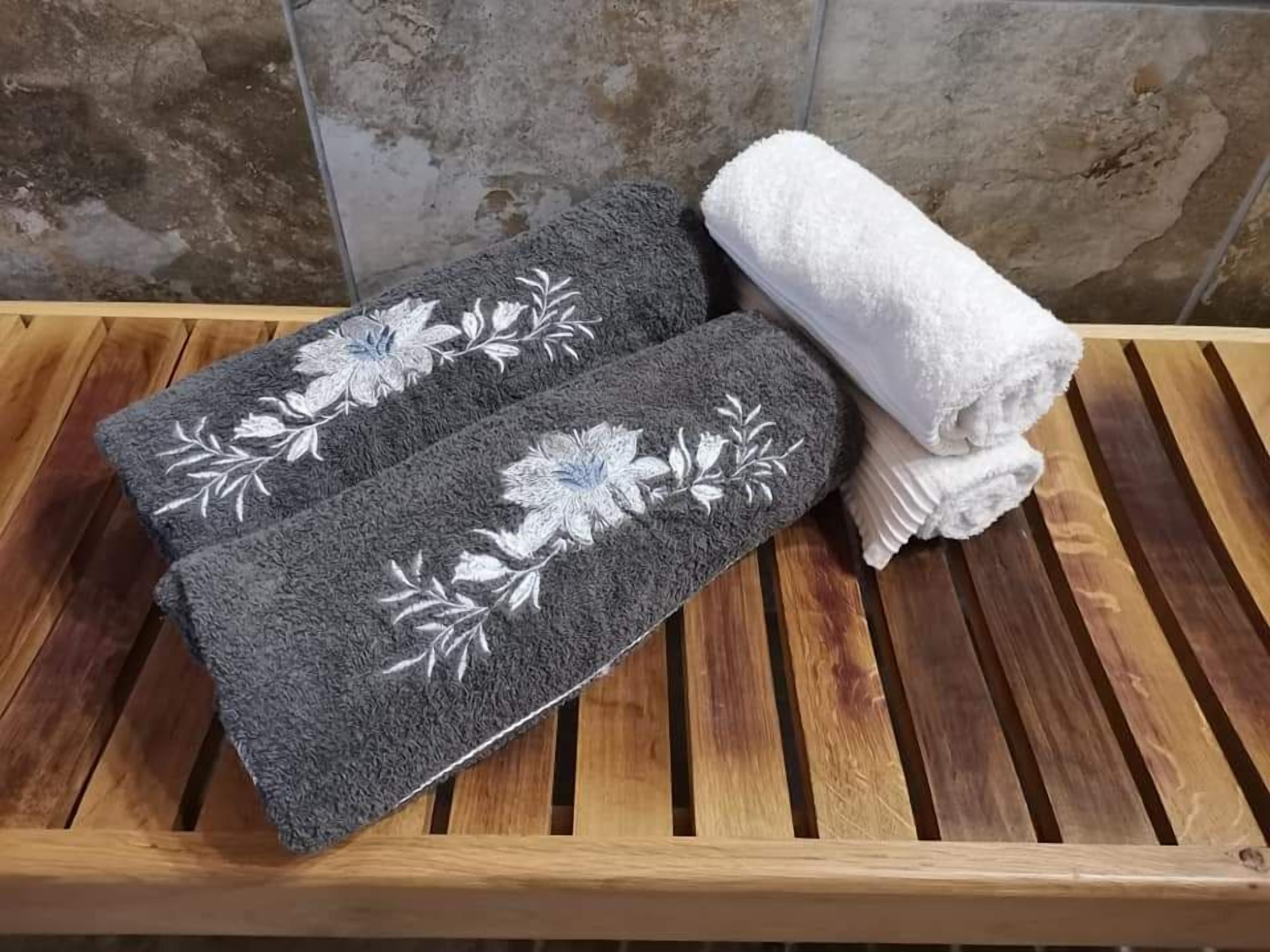 Un banco de madera con dos toallas gris oscuro con bordado floral blanco y una toalla blanca doblada cuidadosamente.