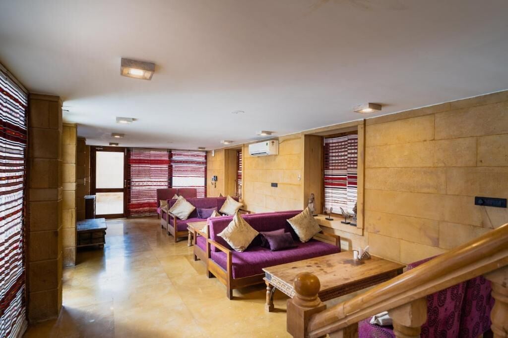 A hotel lobby with a wooden floor, purple sofas with cushions, a wooden table, and a staircase.