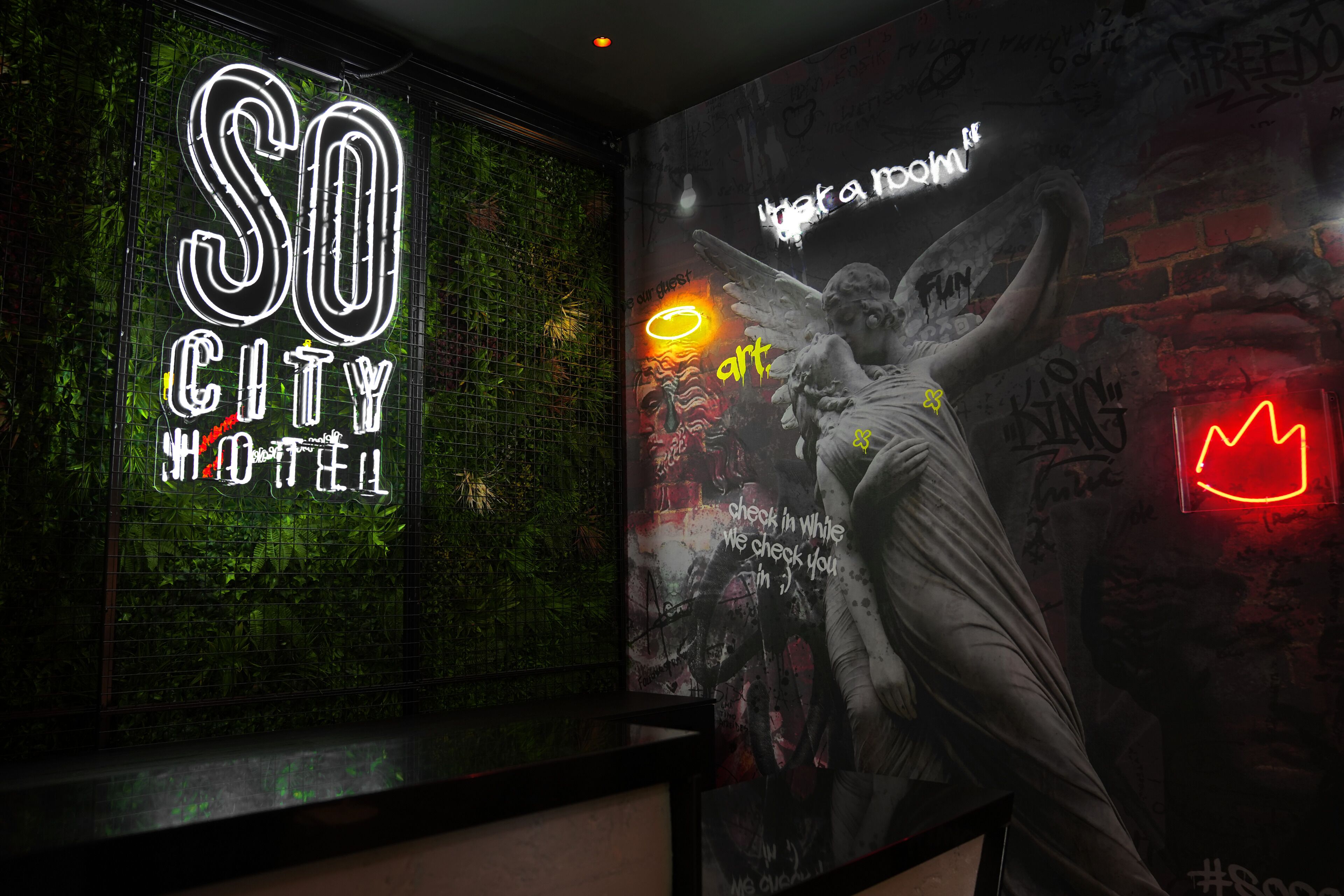 Une enseigne au néon indiquant « SO CITY HOTEL » et une fresque représentant un ange et des graffitis.
