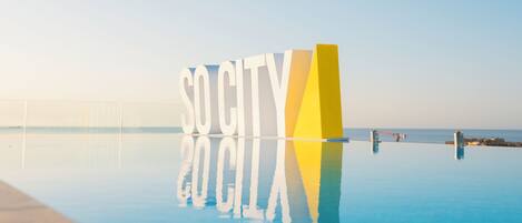 Une piscine dans laquelle se reflète le texte « SO CITY 20 CILA » et un ciel dégagé.