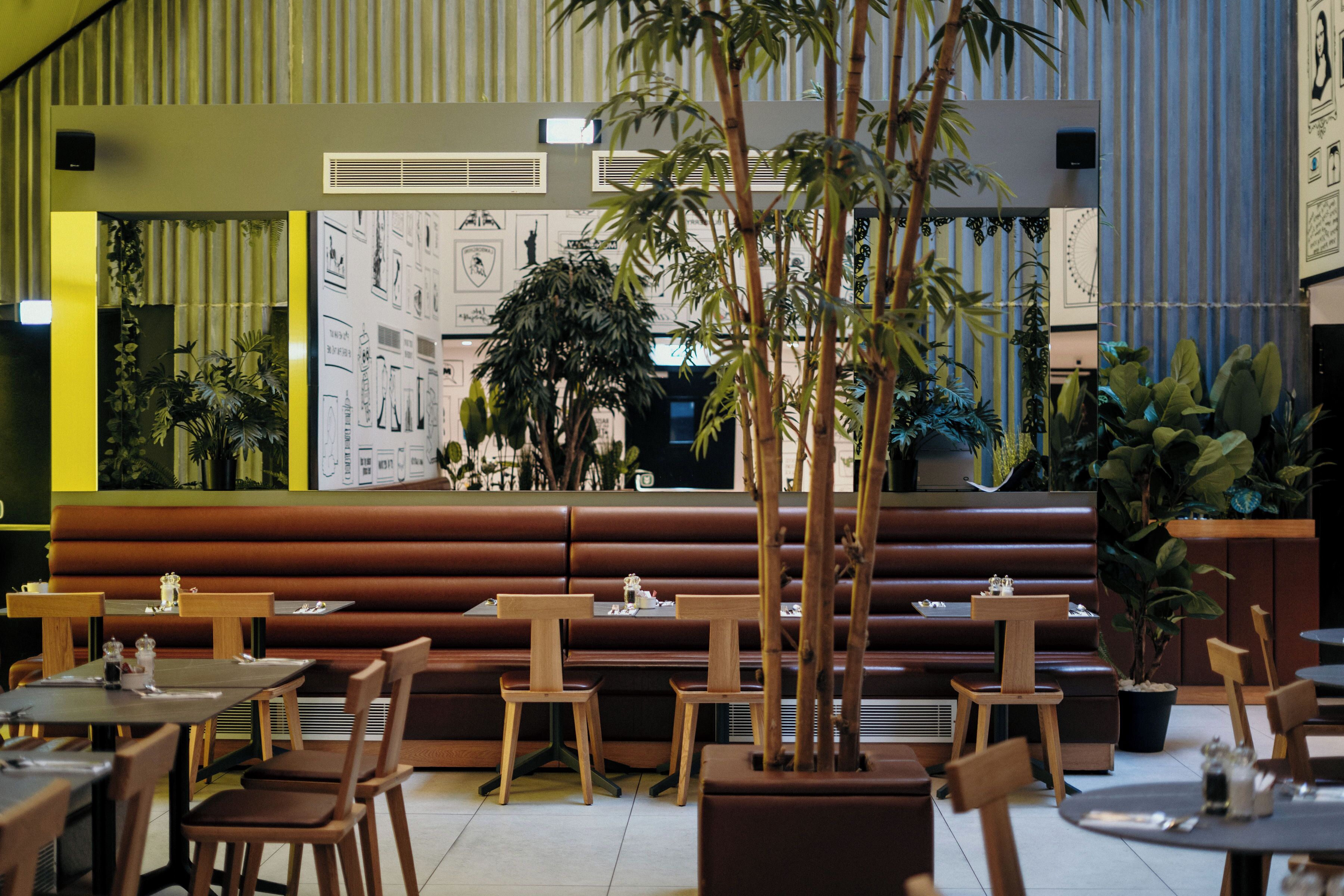 A restaurant with wooden tables and benches, potted plants, and a wall with various designs.