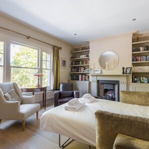 A bedroom with a large bed, a fireplace, a bookshelf, and a window with curtains.