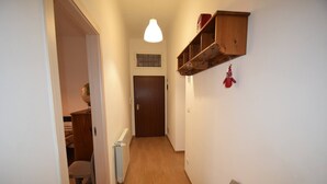 Un pasillo estrecho con suelo de madera, un radiador, una puerta al final y un estante con ganchos en la pared.