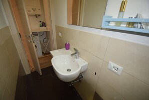 A bathroom with a white sink, a mirror, and a shelf with toiletries.