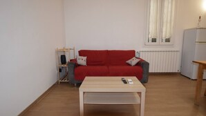 Una sala de estar con un sofá rojo, una mesa de centro de madera, un radiador y una ventana con cortinas.