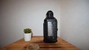 Un farol negro, una pequeña suculenta en maceta y una concha marina sobre una superficie de madera.