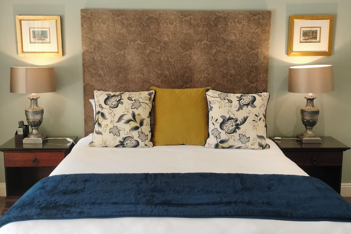 Ein Bett mit blauer Decke, einem braunen Kopfteil und Kissen mit Blumenmuster. Es gibt zwei Nachttische mit Lampen und Dekoration.