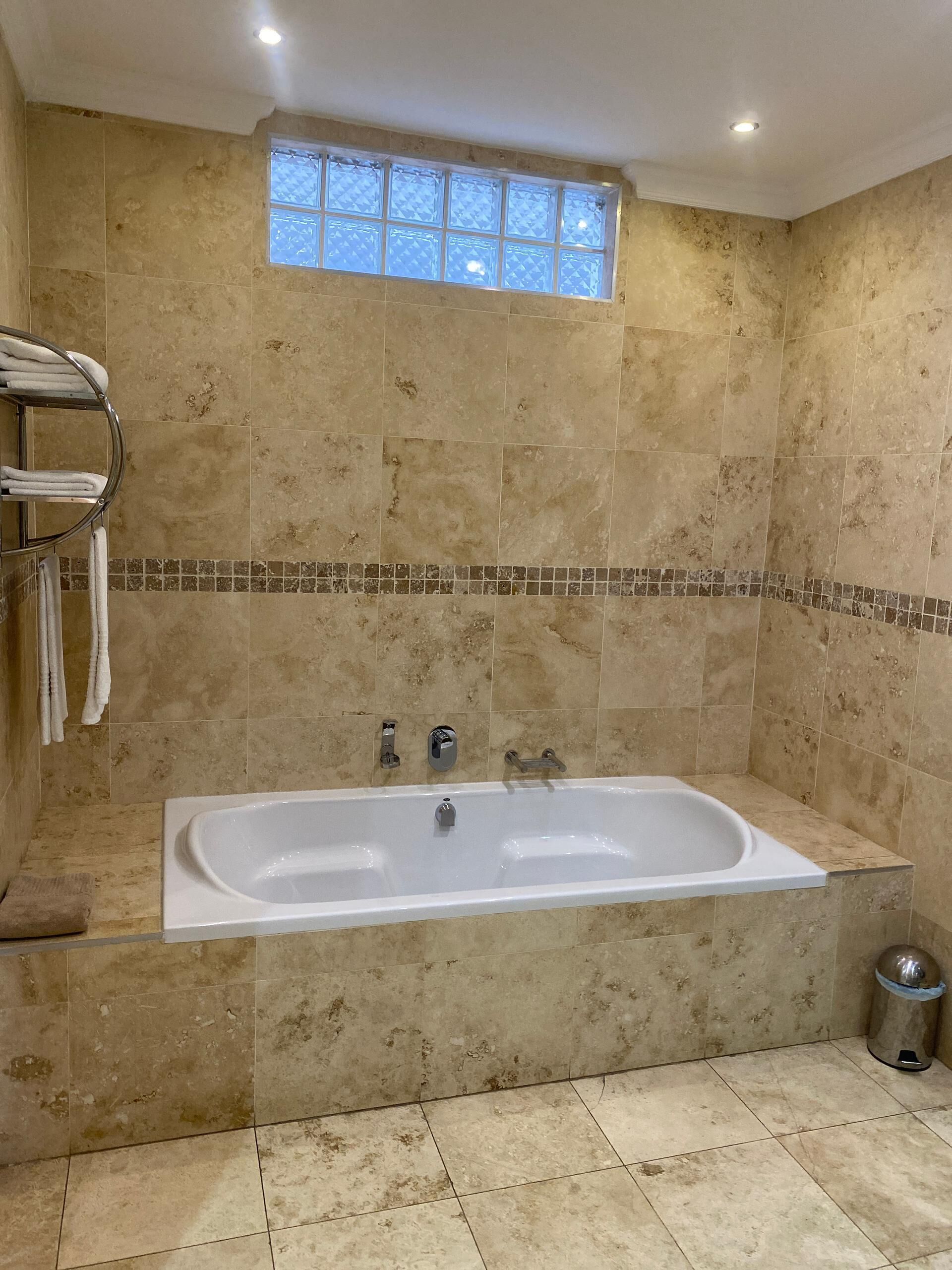 Ein Badezimmer mit einer großen Badewanne, gefliesten Wänden, einem Fenster und einem Handtuchhalter.