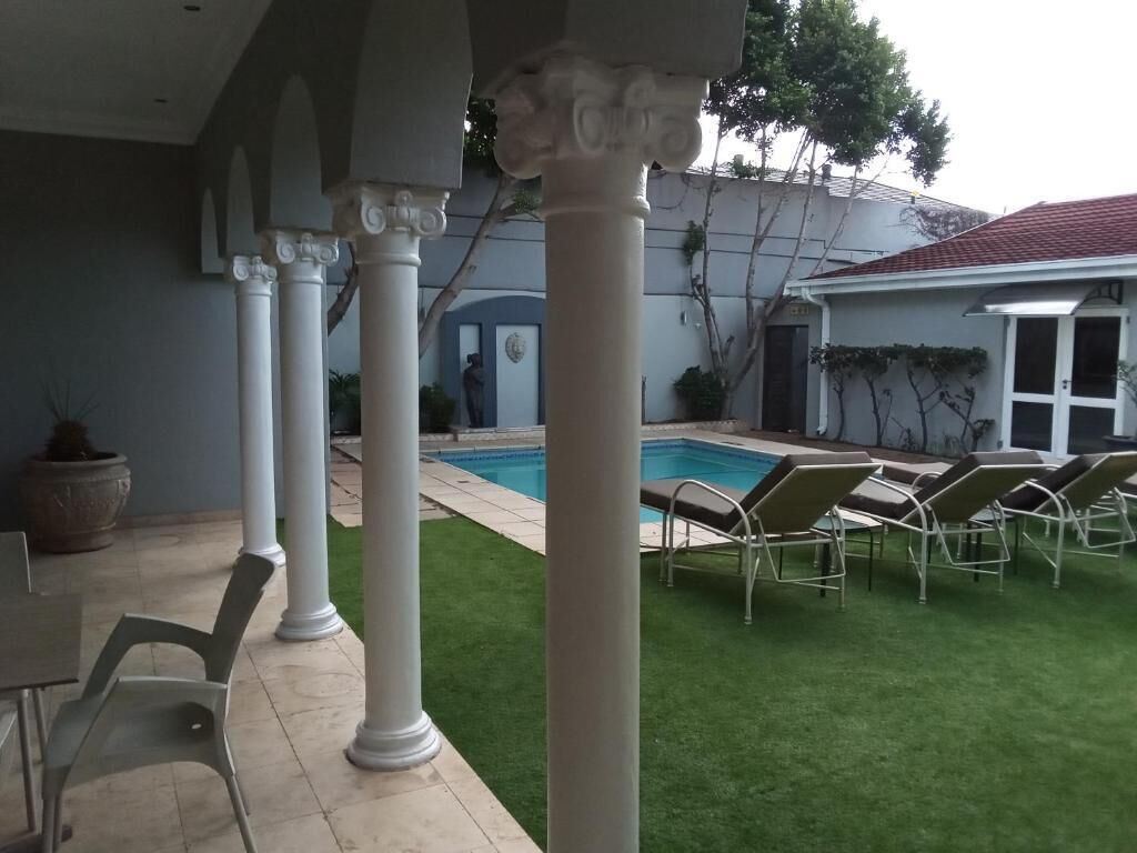 A covered outdoor area with a pool, lounge chairs, and a well-maintained lawn.
