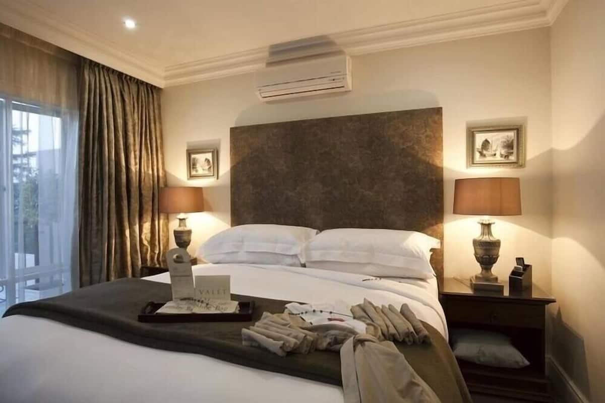 Ein Hotelzimmer mit einem großen Bett, zwei Nachttischen mit Lampen, Blick ins Freie und einer Klimaanlage.