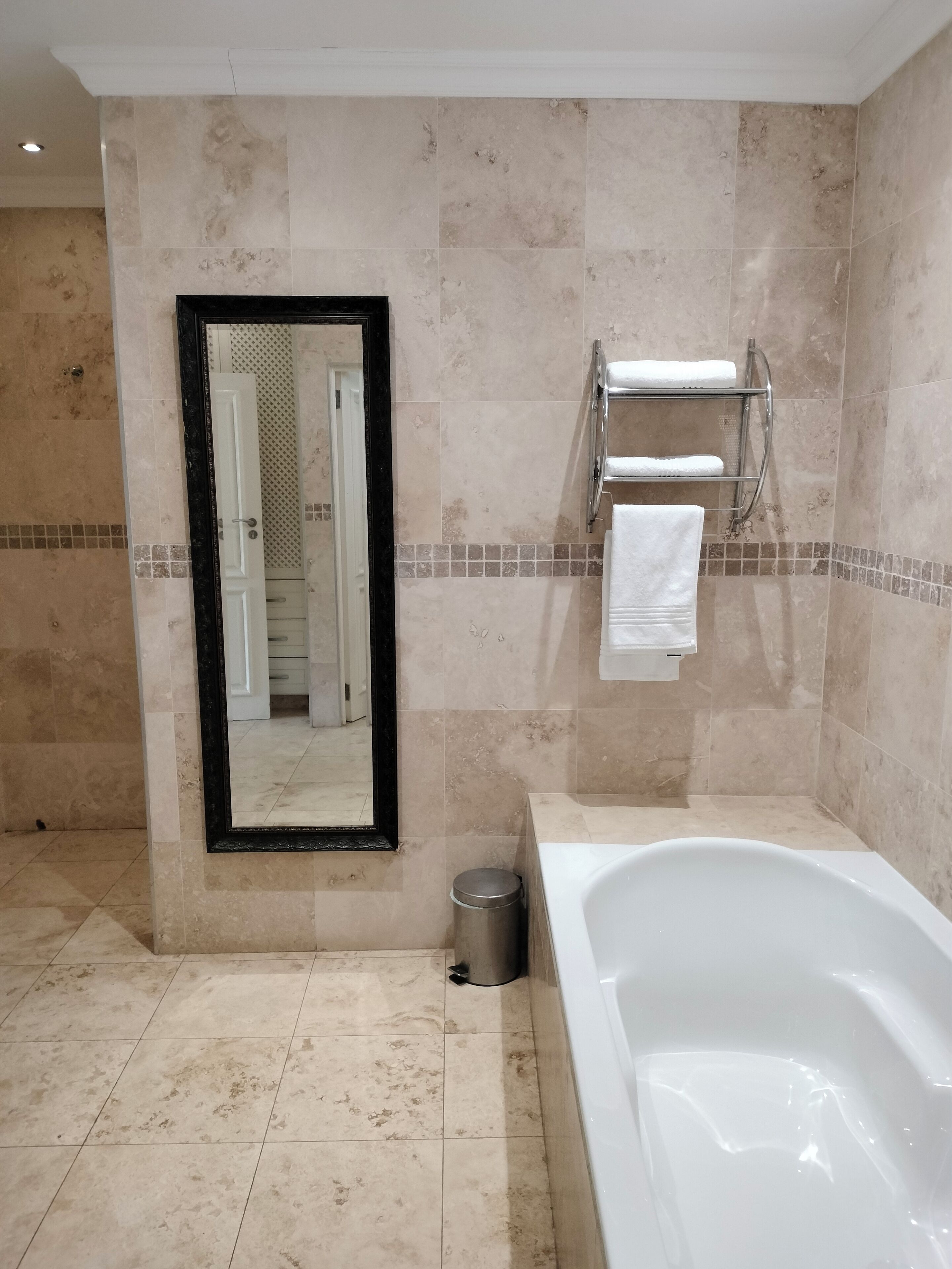 A modern bathroom with a large bathtub, a mirror, and a towel rack.