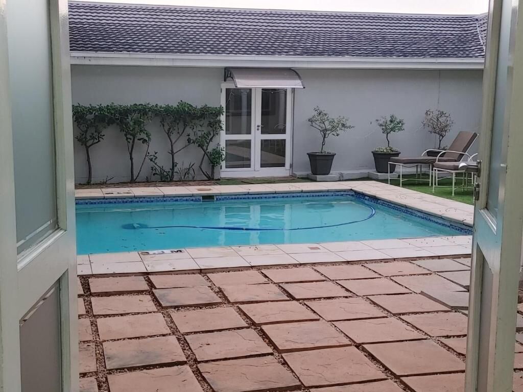 A swimming pool with a tiled deck, a door with a glass panel, and potted plants.