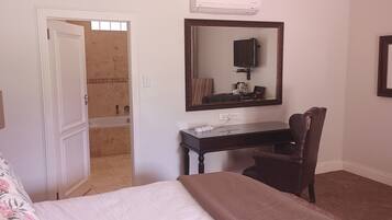 Quarto de hotel com uma cama, uma escrivaninha com cadeira, espelho, televisão e um quadro na parede.