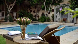 A poolside area with a lounge chair, a book, and a vase with flowers. - 131 on Herbert Baker Boutique Hotel (Pretoria)