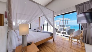 Ein modernes Schlafzimmer mit einem Himmelsbett, einem Nachttisch mit Lampe und Meerblick durch große Fenster.