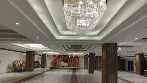 A spacious hotel lobby with a central stage, elegant chandeliers, and a polished marble floor.