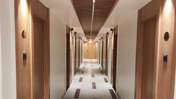 A long, narrow hallway with wooden doors on either side, a marble floor with black and white stripes, and a wooden ceiling with a central light fixture.