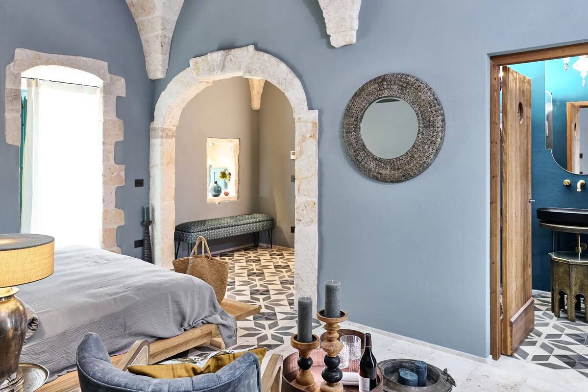 A room with a bed, a bench, a wall-mounted mirror, and a patterned floor.
