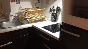 A kitchen with black cabinets, a stainless steel sink, a wooden drying rack, and a clock displaying 17:40.