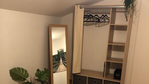 A bedroom with a bed, a large mirror, a wardrobe with shelves, a potted plant, and a hanging plant.