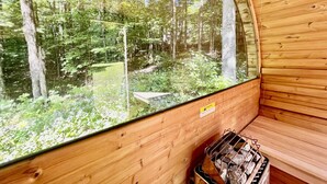 Un sauna en bois doté d’une grande fenêtre donnant sur une zone boisée.