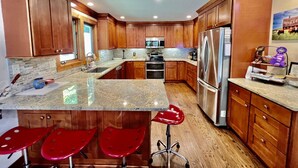Une cuisine moderne avec des meubles en bois, des plans de travail en granit, des appareils électroménagers en acier inoxydable et des tabourets de bar rouges.