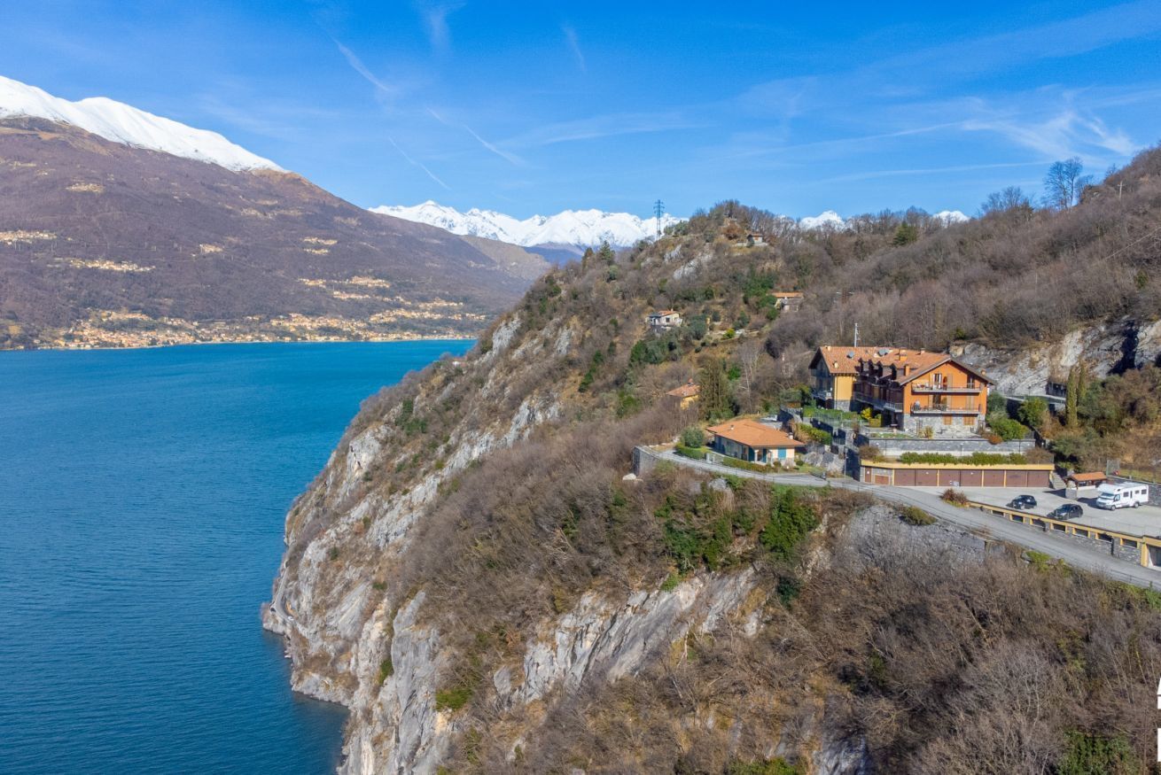 A coastal property with a mountain backdrop, featuring a main building with a sloped roof and a smaller structure nearby.