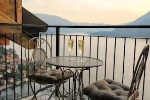 Un balcone con un tavolo rotondo e due sedie, vista su un corpo d'acqua e montagne.