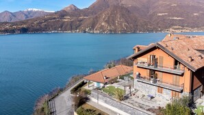 Une propriété située au bord du lac, dotée d’une façade en pierre, d’un balcon avec coin salon extérieur et offrant une vue sur le lac et les montagnes.