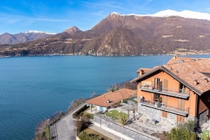 Ein See-Anwesen mit Stein-Fassade, einem Balkon mit Sitzgelegenheit und Blick auf See und Berge.