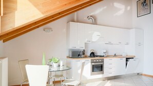 Une cuisine moderne avec des meubles blancs, un four à micro-ondes, une bouilloire et un coin repas comprenant une table et des chaises en verre.