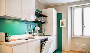 A compact kitchen with white cabinets, a green backsplash, and a window with blinds.