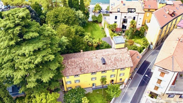 An aerial view of a residential area with a yellow building, a road, and a body of water in the background. - CASA VECCHIA 3 by Design Studio (Bellano)