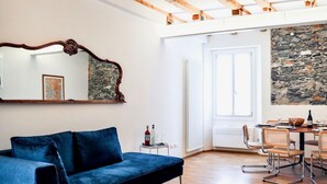 A modern living room with a blue sofa, a dining table with chairs, a stone wall, and a large mirror. - CASA VECCHIA 3 by Design Studio (Bellano)