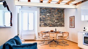 A modern kitchen with a stone wall, wooden beams, a dining table with chairs, and a built-in oven. - CASA VECCHIA 3 by Design Studio (Bellano)