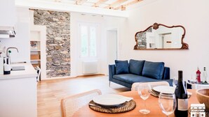 A modern living room with a stone wall, a blue sofa, and a wooden dining table set with plates and wine glasses. - CASA VECCHIA 3 by Design Studio (Bellano)