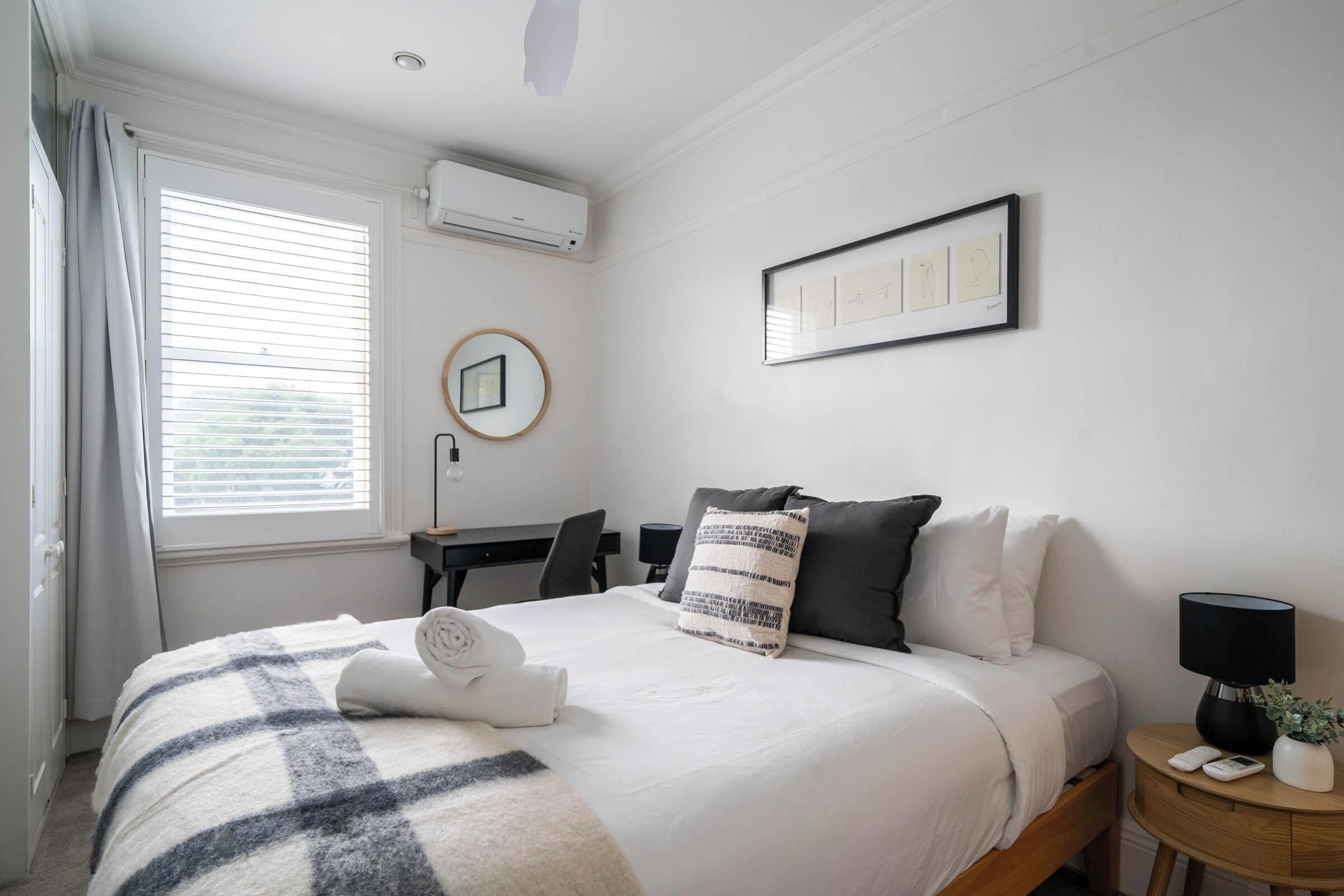 A neatly arranged hotel room with a bed, bedside table, and a desk with a chair.