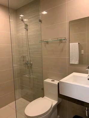 A modern bathroom with a glass-enclosed shower, a white toilet, and a sink with a mirror above it. - Mactan Newtown A by HiveRooms (Lapu-Lapu)