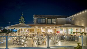 An outdoor dining area with tables and chairs, a building with a tiled roof, and a night sky. - Amaryllis Hotel (Zakynthos)