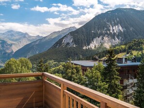 Ett bergigt landskap med en träveranda som vetter ut mot en by med traditionella byggnader och erbjuder utsikt över bergen.