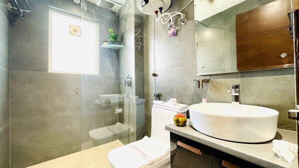 Un baño moderno con ducha envuelta en vidrio, un lavamanos blanco y un mueble de tocador de madera.